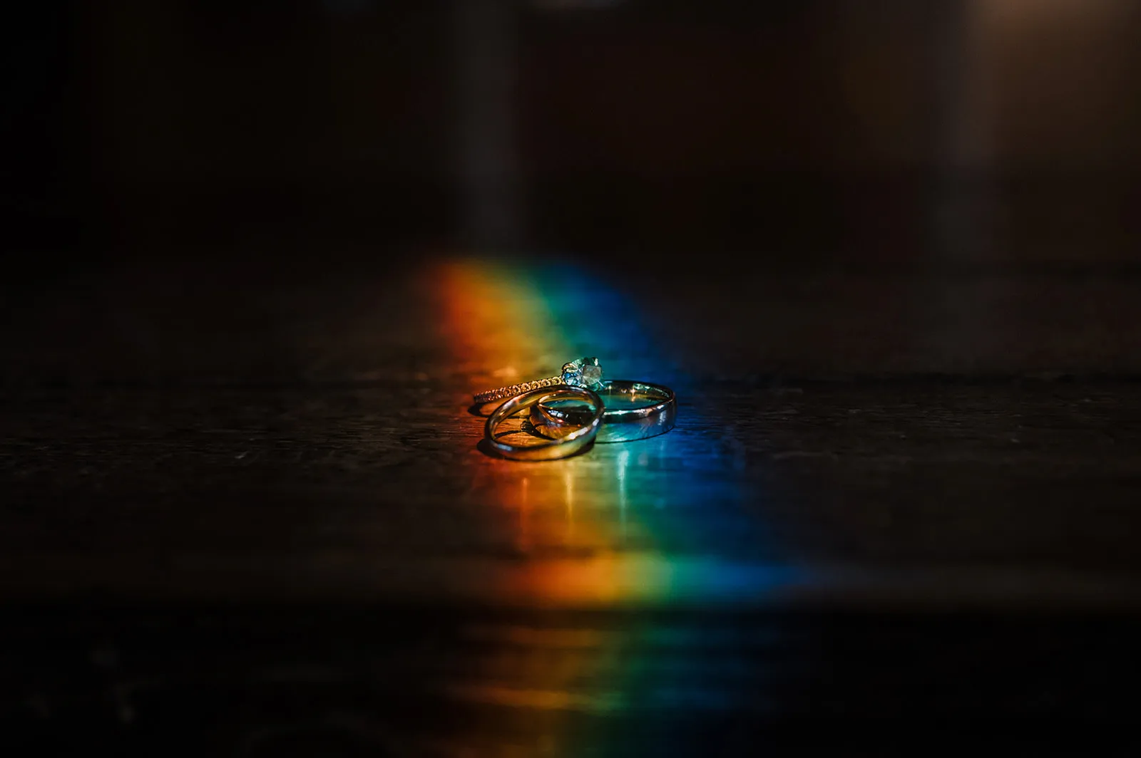 Close-up of the three wedding rings resting on a dark surface, lit by a rainbow of refracted light